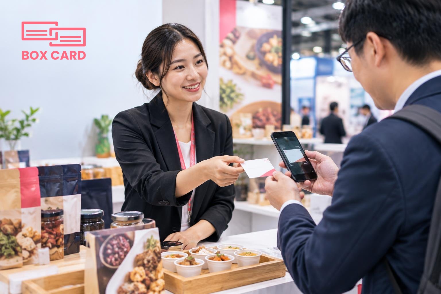 Exhibitor handing a business card to an importer at a Hong Kong trade show booth, product samples on the table and a smartphone scanning the card, editorial photograph