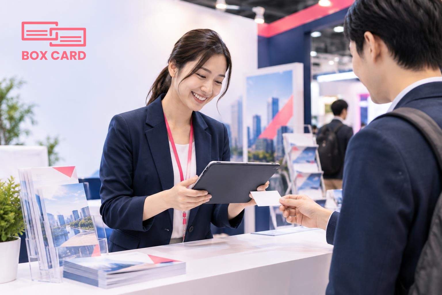 พนักงานขายใช้แท็บเล็ตสแกนนามบัตรบนเคาน์เตอร์บูธ งานแสดงสินค้ามีสแตนด์และโบรชัวร์เป็นฉากหลัง